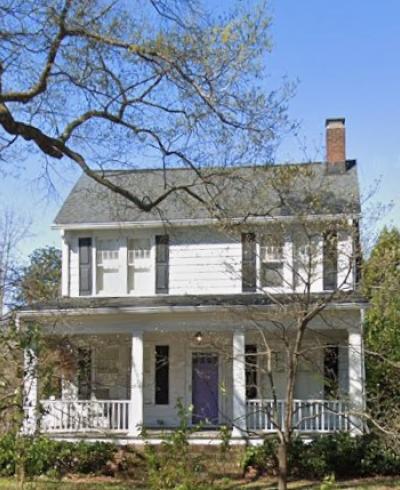 Front of two-story white house with front porch, black shutters, and chimney